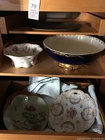 Photo showing four decorative porcelain bowls arranged on wooden shelves including a large cobalt blue bowl and three smaller floral patterned bowls.