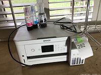 Front view of Epson EcoTank printer with ink bottles and power cords on top