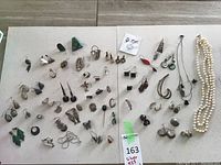 Wide overhead view showing full assortment of silver earrings and necklaces arranged on white surface