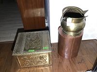 Overview photo showing metal box in front and metal pitcher on cylindrical stand behind, positioned on wood floor.