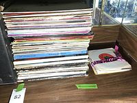 Stack of vinyl records and a small pile of loose records with pink and black tape on sleeves