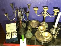 Photo showing an assortment of candelabras, bells, small serving tray and egg coddlers