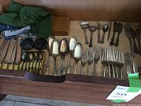 Wooden drawer with assorted flatware including forks, spoons, yellow-handled knives, salt cellars and serving utensils