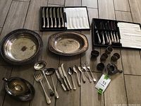 Full lot display showing two boxed sets of knives, trays, assorted spoons, forks, small cups, and decorative pieces