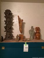 Full view of multiple statues and clay crosses arranged on surface including tall clay figure sculpture, wooden hand statue, and clay figurines.