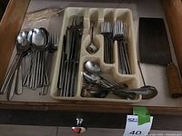 Drawer with stainless steel spoons, forks and knives, plastic utensil tray, and wooden-handled cleaver knife.