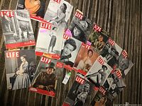 Photo showing 15 vintage Life magazines laid out on carpet, covers including women in dresses, military personnel, and various portraits
