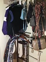 Hanging women's clothing items and several purses and bags on hooks and rod, shown are tops, sweaters, patterned pants, and handbags in colors ranging from black, gray to tan and blue.