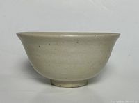 Side view of the antique ceramic bowl showing the light beige glaze and speckled details.
