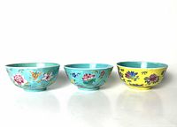Front angle of three famille rose porcelain flower bowls, two turquoise and one yellow, decorated with flowers and butterflies.