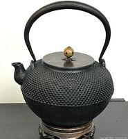 Front view of the black Japanese iron teapot on a black surface showing spout, handle, lid with brass knob, and textured surface.