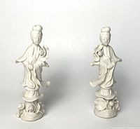 Front view of two white porcelain Kwan Yin statues on lotus bases with flowing robes.
