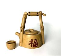 Front side view of the Yixing Zisha teapot showing bamboo-style handle, textured body, and Chinese character on body, alongside the matching clay cup.