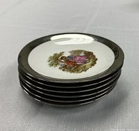 Stack of six porcelain plates with black rims and central artwork showing a couple under a tree
