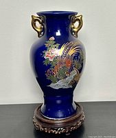 Full view of the blue vase with stand under showing its shape, gold handles, and painted floral and bird decoration.