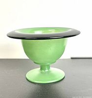 Side view of the green jade glass bowl showing its pedestal base, rounded bowl shape, and black rim.