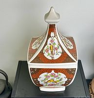 Front and side view of the square jar with lid showing bird and flower panels, red and gold decorative background.