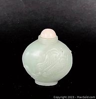 Front view of white and light green nephrite jade snuff bottle with a carved motif and pale stopper on a black background.