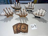 Five wooden model ships and three vintage wooden ship-themed coasters arranged on a white surface, showing the overall lot contents.