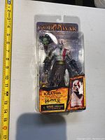 God of War Kratos action figure in sealed blister pack with a ruler indicating size.