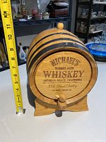 Mini whiskey barrel with detailed front label showing brand and location, with measuring tape showing height around 9 inches.