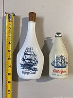 Photo of two vintage cologne bottles: Flying Cloud and Old Spice after shave lotion with ship illustrations and a tape measure showing their size.