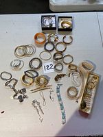 Wide shot showing all assorted costume jewelry items including bracelets, earrings, keychain, and watch on white table.