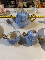 Blue glaze tea pot, creamer, and sugar bowl with gold handles and lids shown, display of three main tea set pieces.