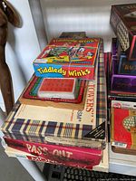 Photo showing stacked board games including 'Tiddledy Winks', 'Monopoly Pass-Out', and 'Towers' with some visible wear and discoloration on boxes