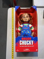 Bride of Chucky doll in original packaging with a measuring tape to show size, box shows minor damage and wear.