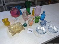 Overview of 15 colorful glass vases, bowls, and candy dishes in various colors on white table