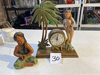 Photo showing both the Polynesian sitting girl statue and the pin-up girl mantel clock with palm tree decorations on a table.