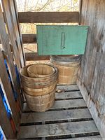 Three wooden bushel baskets stacked together with a light green wooden crate on top, photographed outdoors in a wooden structure.