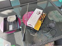 Barbecue tools, rotisserie kit, baking pans and skewer set displayed on glass outdoor table with pink placemats as background.