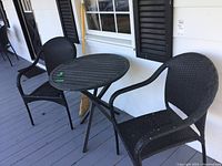 Two black resin wicker style armchairs and one round black folding metal table in outdoor porch setting.