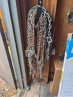 Set of multiple hanging metal chains of different sizes and thicknesses in a wooden shed corner.