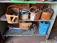 Three wooden baskets on a metal shelf, holding metal chains and other hardware, along with a metal hand crank tool below the shelf and a blue plastic container.