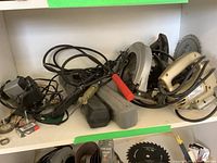 Photo showing collection of tools including circular saw, jig saw, blades, cases, and miscellaneous items on shelving