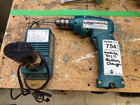 Makita cordless drill and battery charger on a wooden surface.