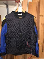 Front view of black quilted heated vest with wiring hanging outside a blue and black motorcycle jacket