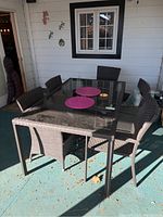 Rectangular resin wicker patio table with glass top and five matching resin wicker chairs on outdoor patio area.