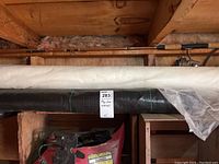 Rolls of black plastic wrap and white garden fabric stored on a wooden shelf under a roof beam with fishing rods above.