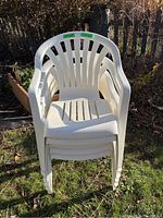 Stack of five white resin patio chairs stacked on grass outdoors, showing the overall set and confirming quantity.