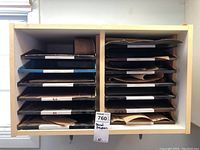 Front view of white wooden cabinet showing 10 shelves filled with a variety of sandpaper sheets in different grits and sizes, some labeled.