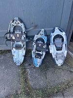 Photo showing two pairs of GV snow shoes leaning against a shed, silver frames with bindings and crampons visible.