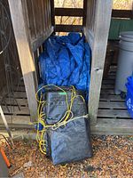 Photo showing the four tarps bundled and placed on a wooden shelf outdoors, with some leaves around the base; tarps appear weathered.
