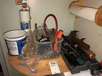 View of plastic container with various small hand tools, hardware, and hammers on wooden surface under paper towel holder