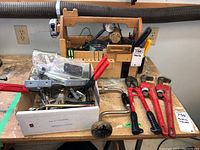 Overview of the tools on a workbench including a wooden tool caddy, clamps, and pipe wrenches.