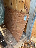 Disassembled wood table top leaning against shed wall with visible wood grain and wear marks.