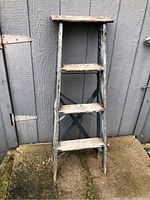 Front view of wood ladder showing four steps and wide top platform with chipped blue paint.